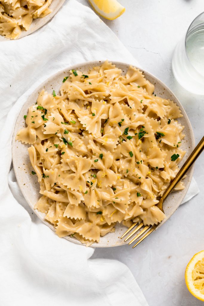 Lemon pasta on a plate sprinkled with parsley and a side fo white wine.