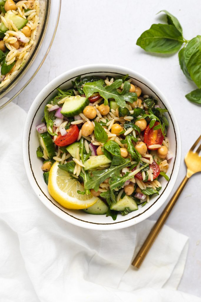 Overhead image of a bowl of orzo salad with basil and a fork on the side.