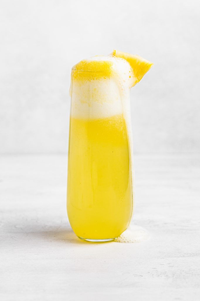 Close up image of pineapple mimosas, garnished with fresh pineapple.