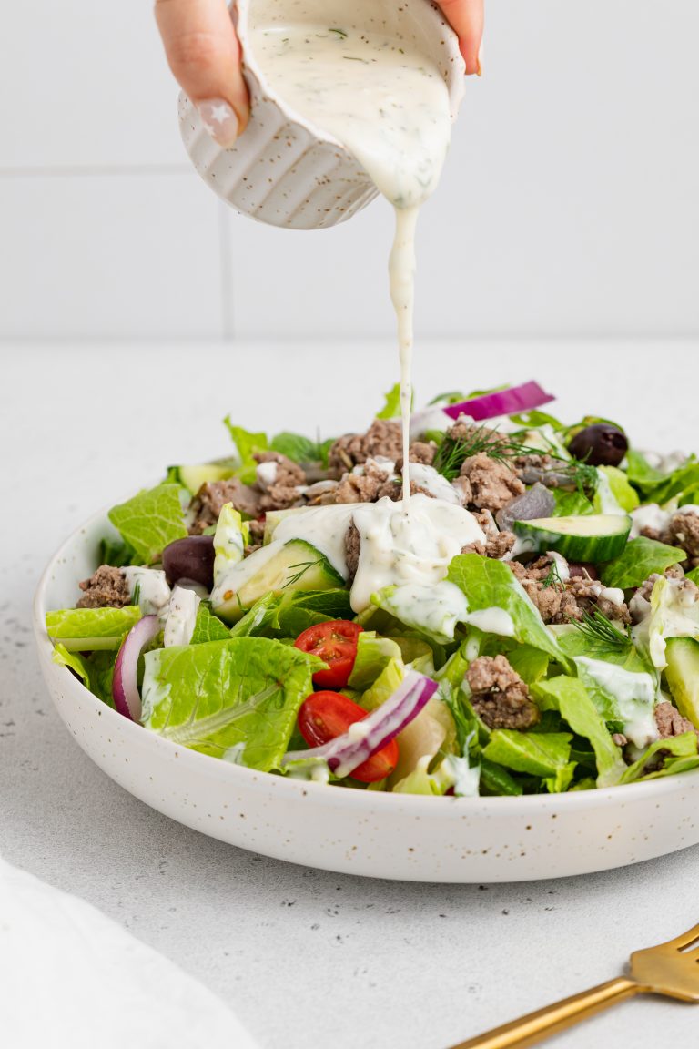 tzatziki dressing being poured over a gyro salad
