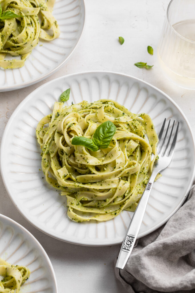 vegan pesto pasta in a bowl with a fork and white wine on the side.