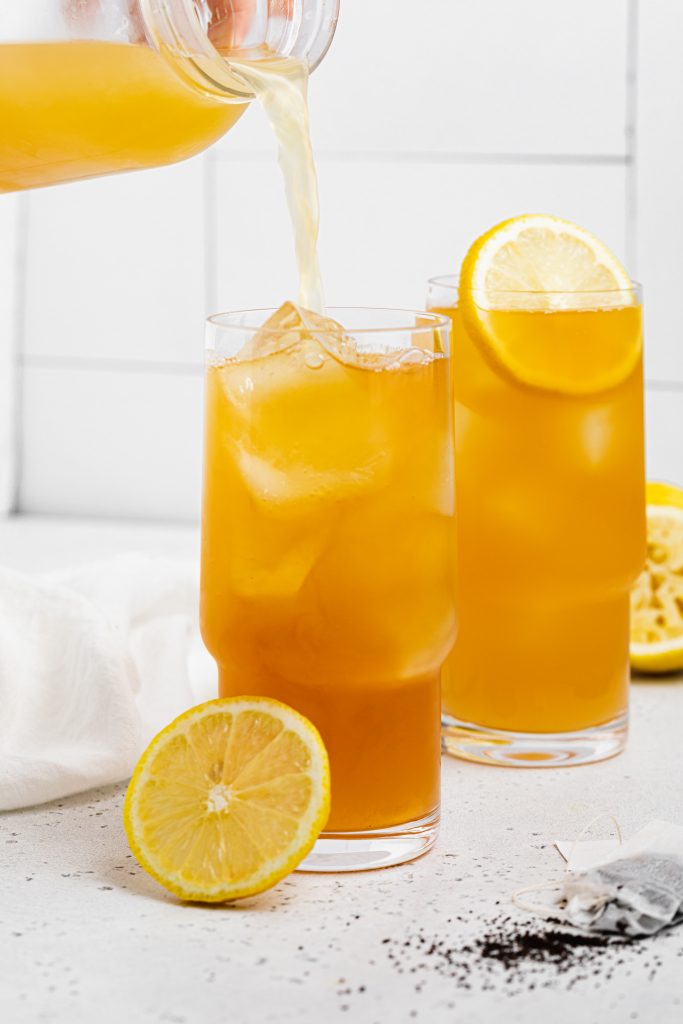 lemonade being poured into a glass of an arnold palmer drink with lemon slices on the side