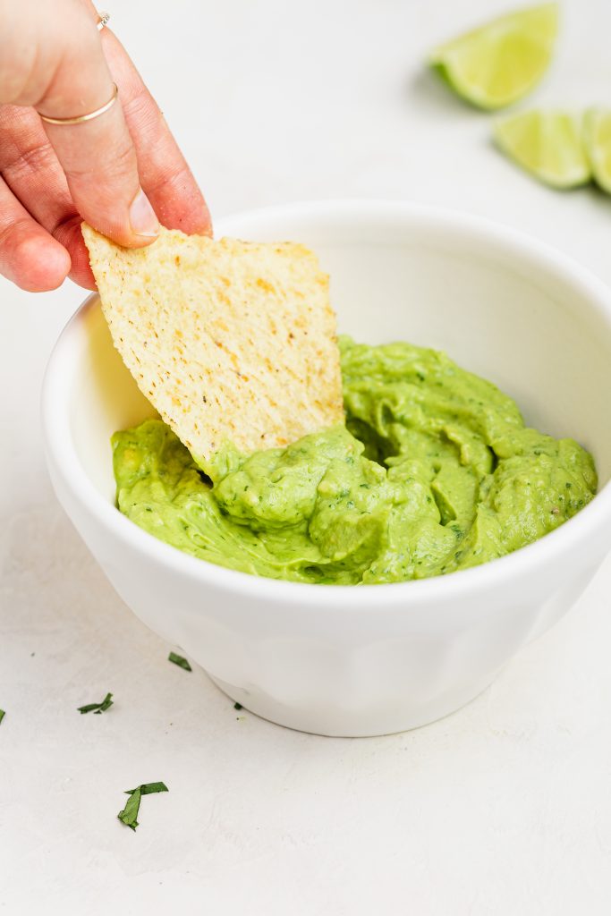 avocado crema being scooped from a bowl with a tortilla chip