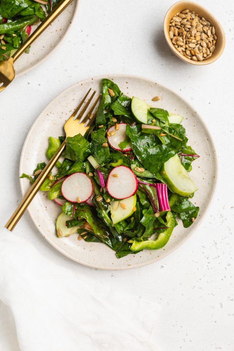swiss chard salad on a plate with a fork and sunflower seeds on the side