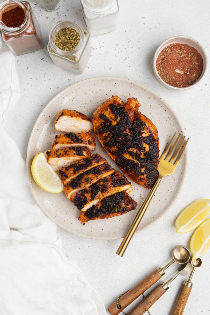 overhead image of blackened chicken on a plate with spices around the plate