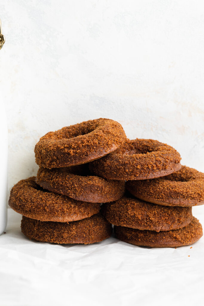 healthy vegan apple cider donuts stacked on top of each other, with a bottle of milk on the side.