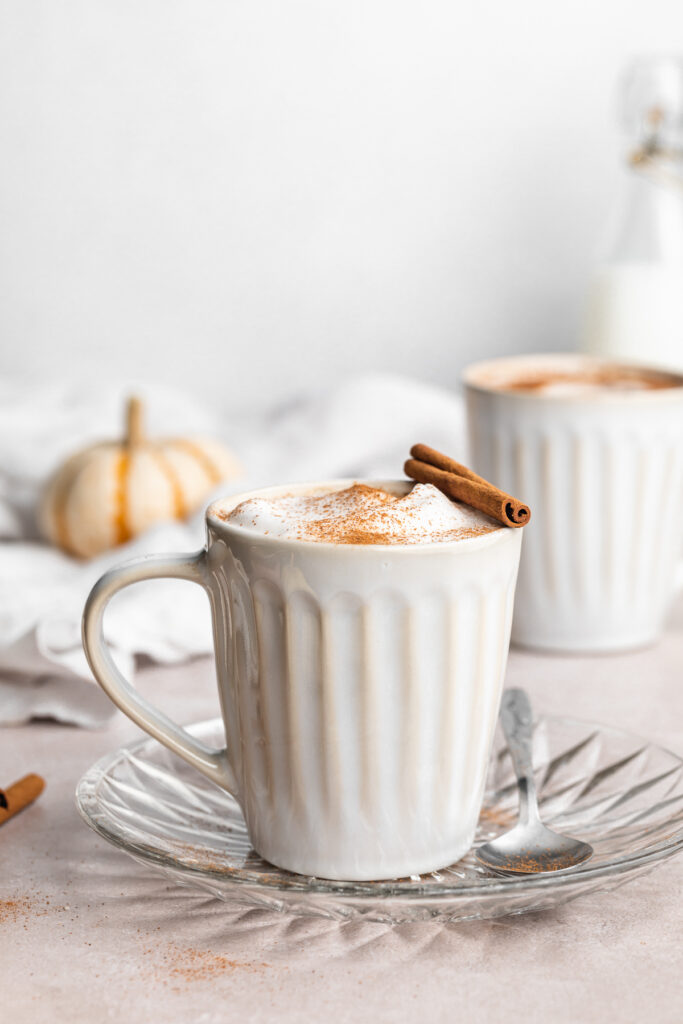 two pumpkin spice lattes in mugs with a mini pumpkin on the side.