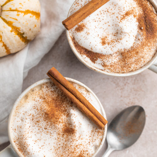 overhead image of two pumpkin spice lattes with cinnamon sticks on top.