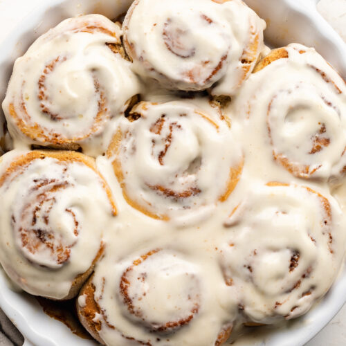 Overhead image of gluten-free cinnamon rolls in a baking dish with cream cheese frosting on top.