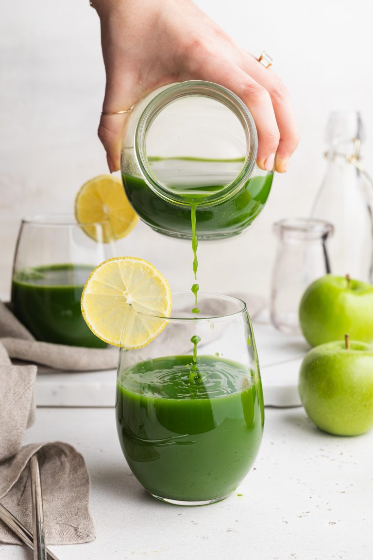 green blender juice being poured into a glass, garnished with a lemon slice