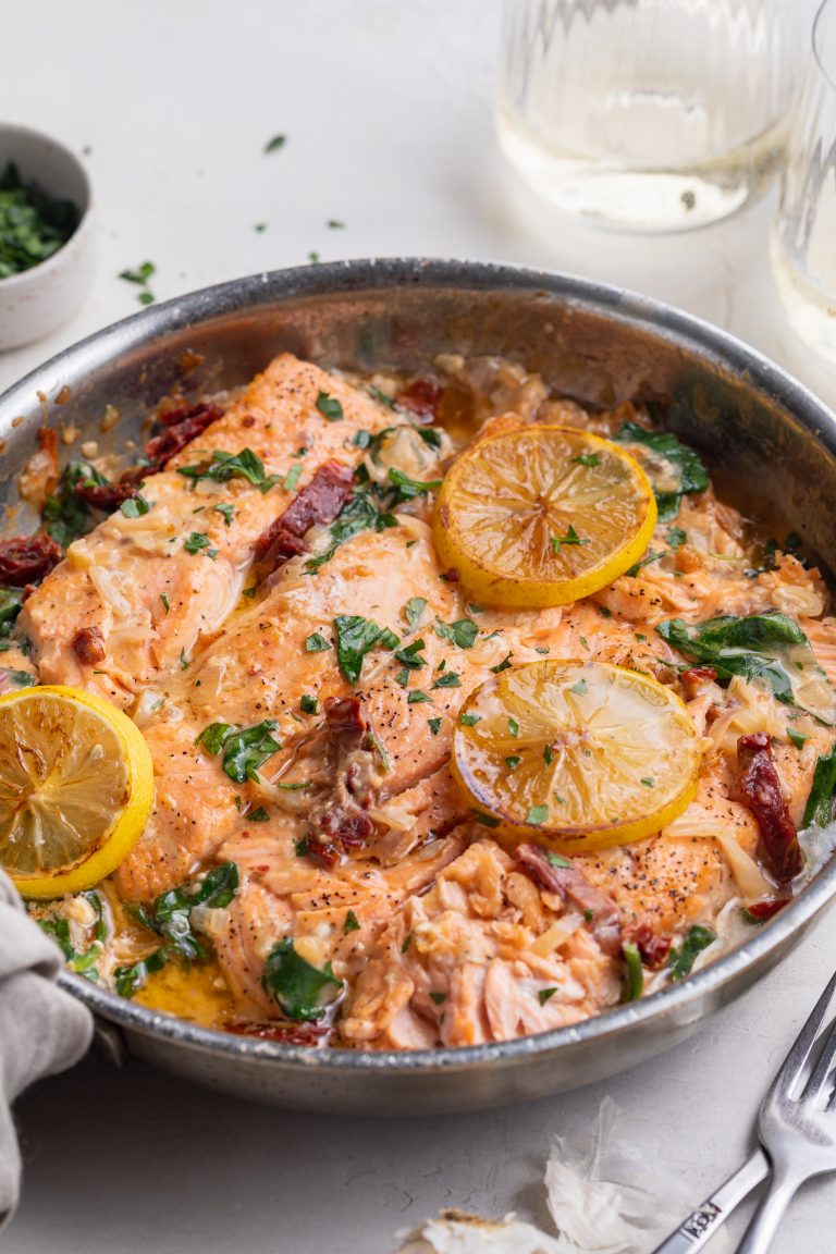 sun dried tomato salmon recipe in a skillet with while wine and fresh parsley on the side