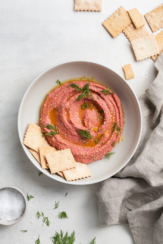 overhead image of roasted beet hummus in a bowl with crackers on the side
