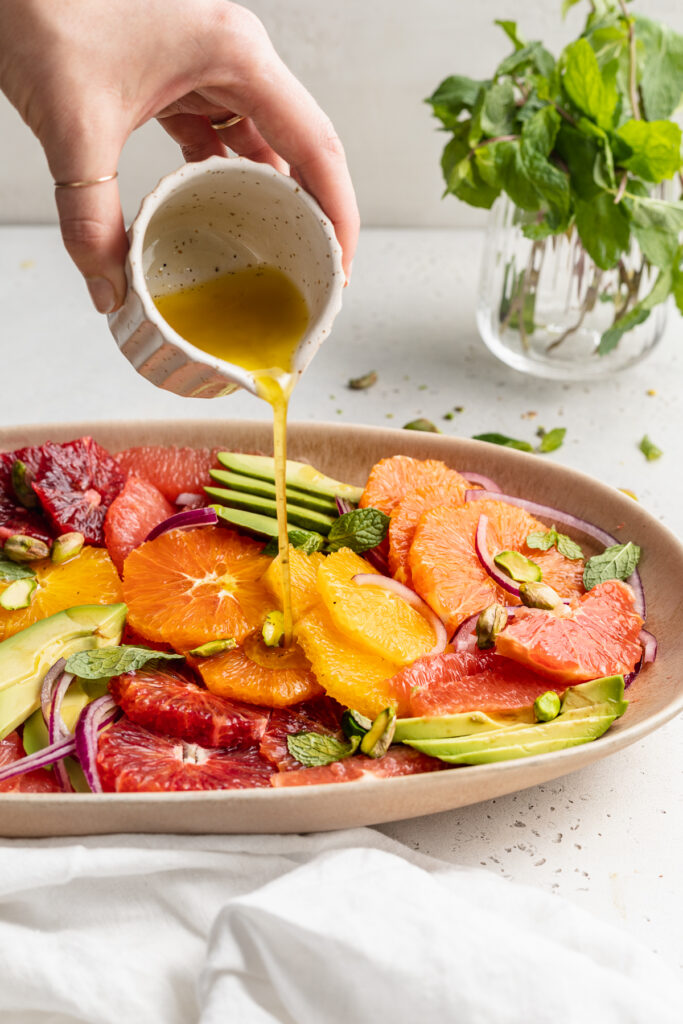 dressing being poured over citrus salad