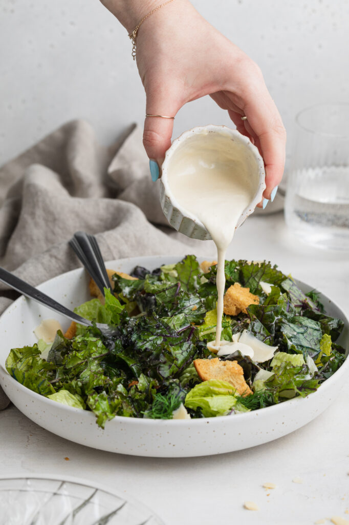 dressing being poured over kale caesar salad