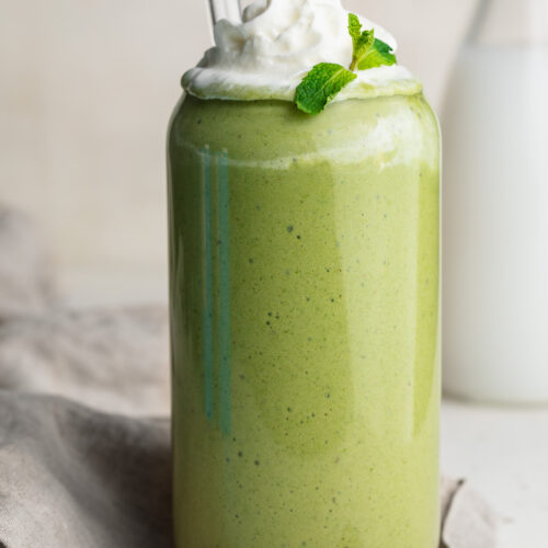 healthy shamrock shake in a glass with whipped cream and fresh mint on top.