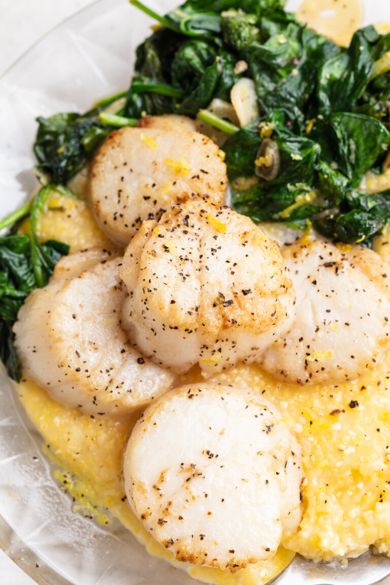 close-up image of seared scallops with polenta and garlicky greens on a plate.