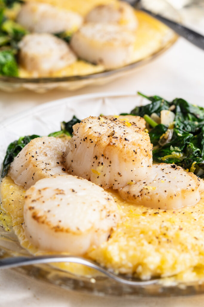 two plates of the seared scallops recipe with garlicky greens and polenta
