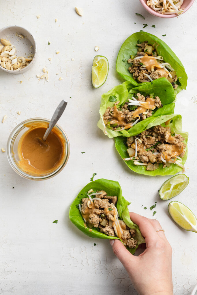 four turkey lettuce wraps on a table, one being picked up.