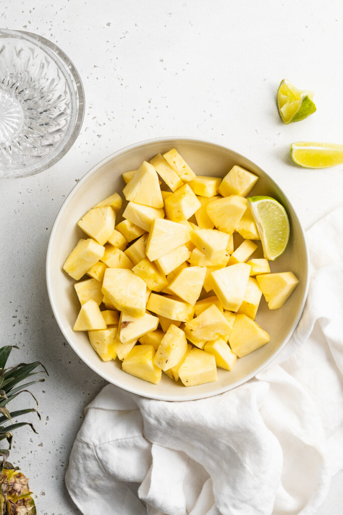 cut pineapple in a bowl with limes on the side