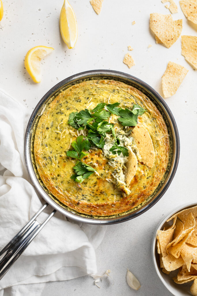 Overhead image of vegan spinach artichoke dip in a skillet with chips on the side.