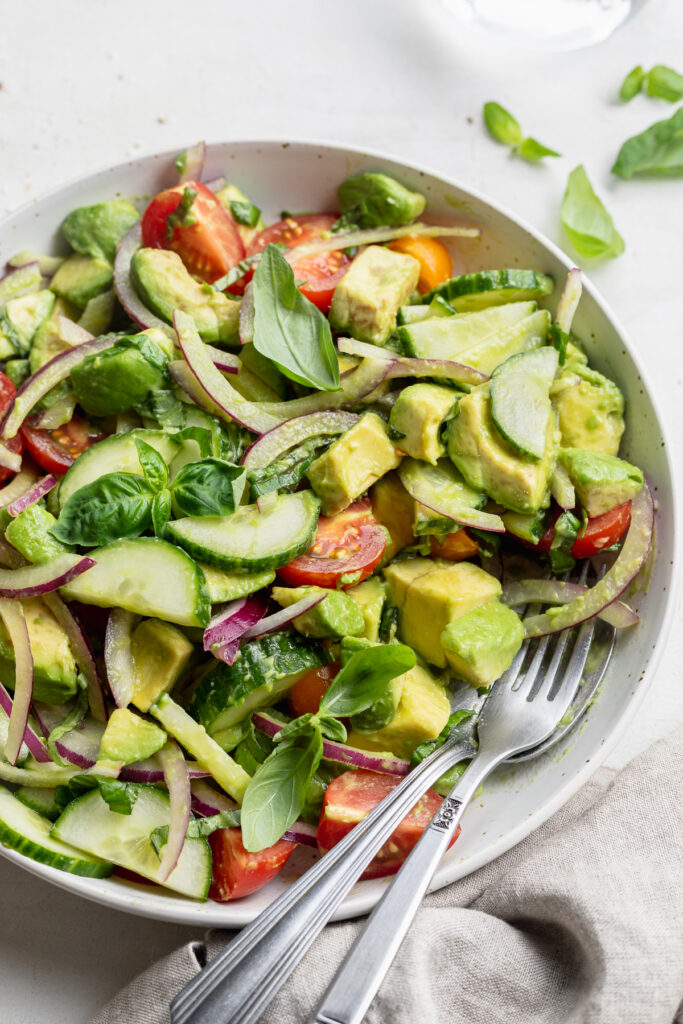 avocado salad in a bowl with serving utensils.