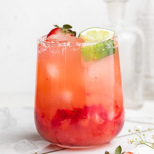 skinny strawberry margarita in a glass with fresh strawberries and lime wedges on top.