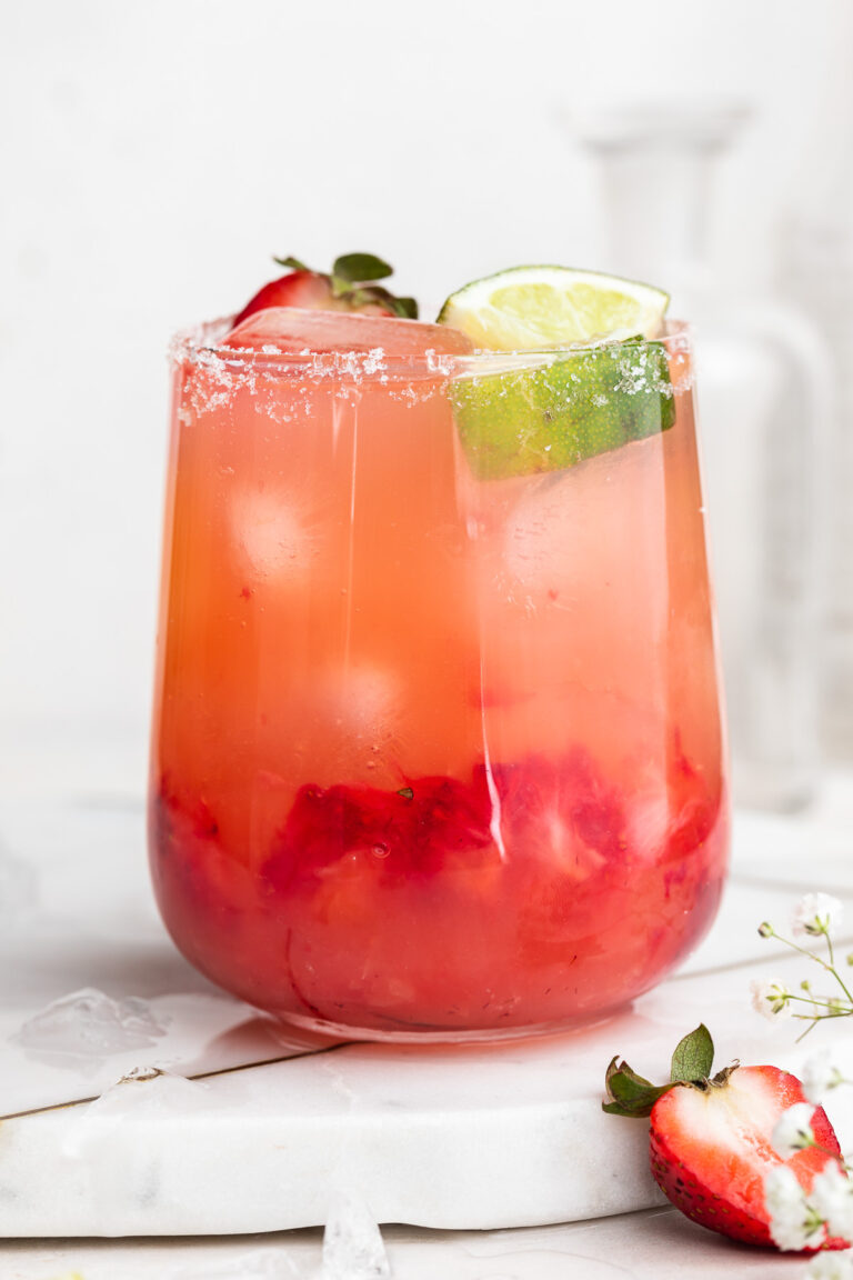 close-up image of a skinny strawberry margarita in a glass with fresh strawberries and lime wedges on top.