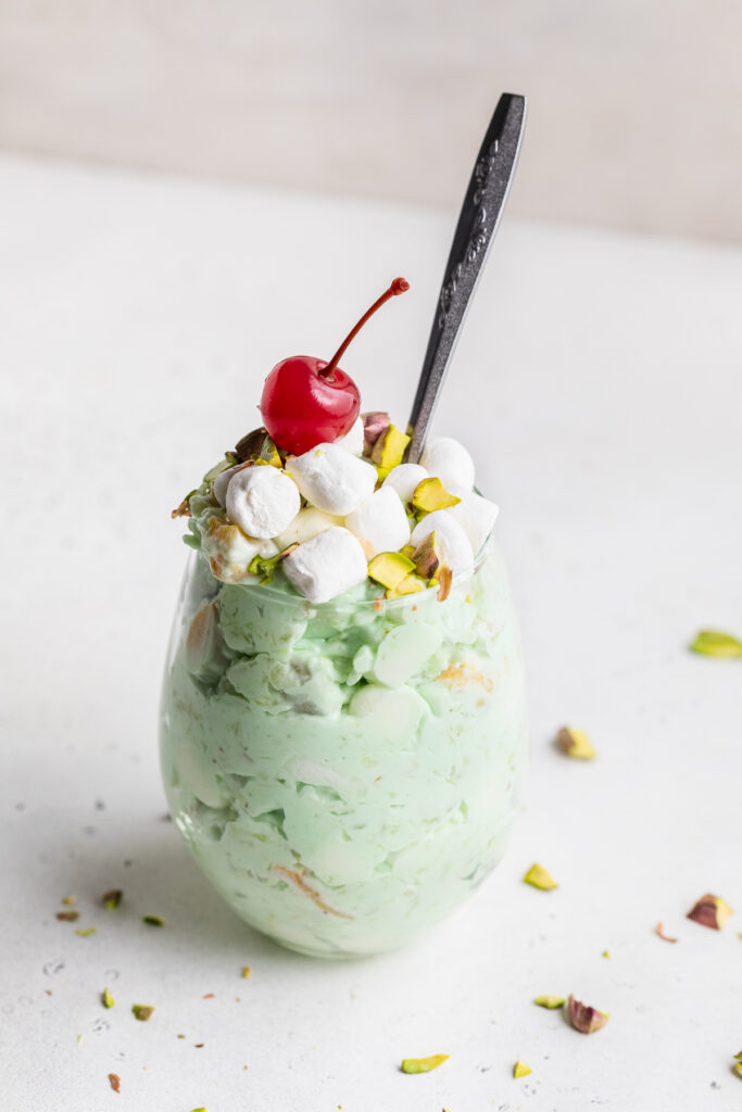 one glass of watergate salad with chopped pistachios and a cherry on top.