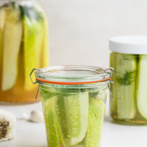 three jars of pickles with garlic and salt on the side.