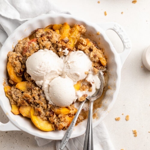 overhead image of peach crisp in a pie dish wtih vanilla ice cream on top.