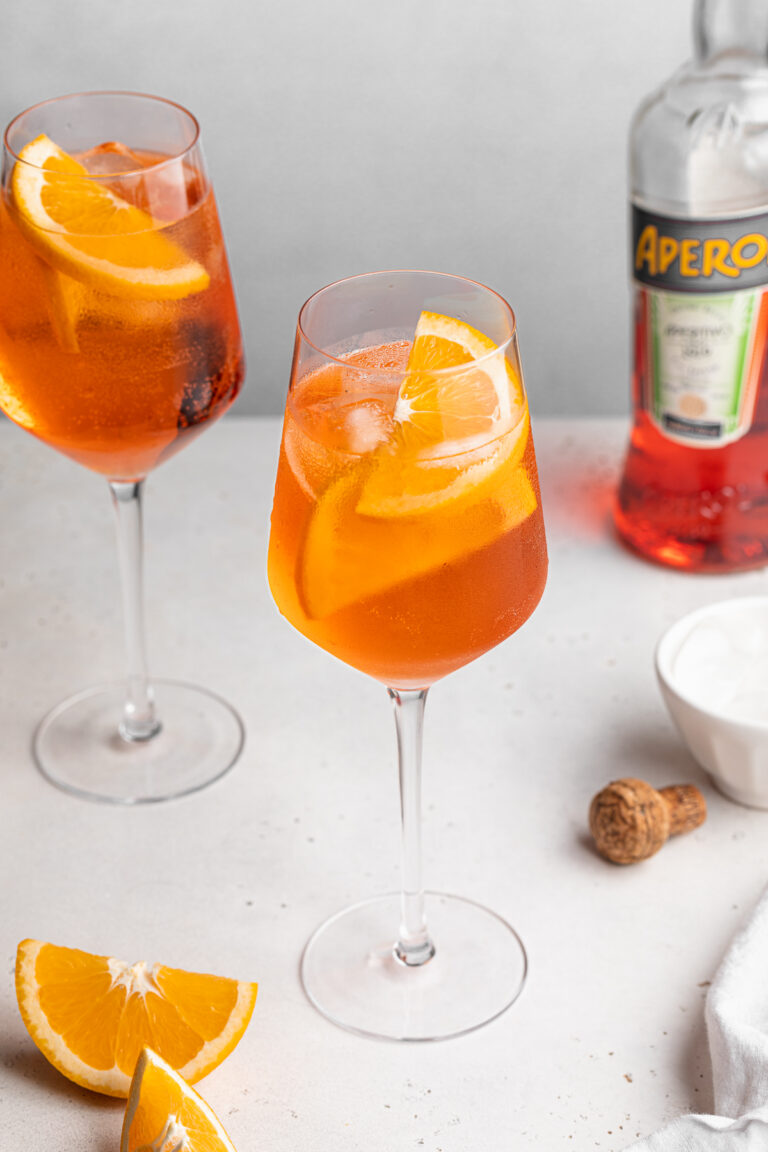 Two aperol spritz in white wine glasses with a bottle of aperol on the side.
