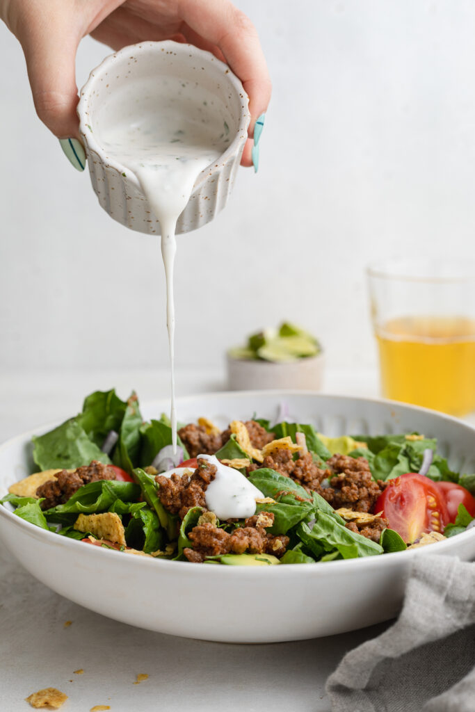 creamy cilantro lime dressing being poured over a taco salad.