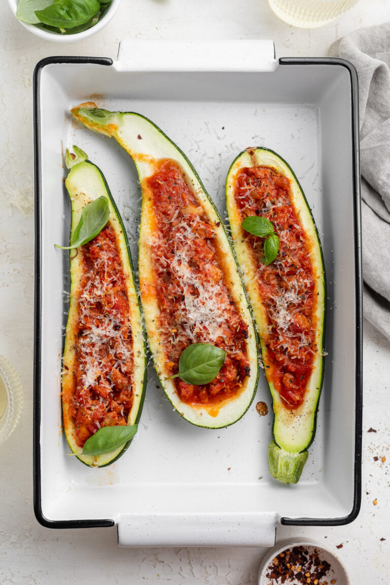close up image of stuffed zucchini boats in a baking dish with fresh basil on top.