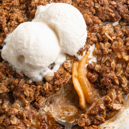 gluten free apple crisp in a baking dish with a spoon and two scoops of ice cream on top.