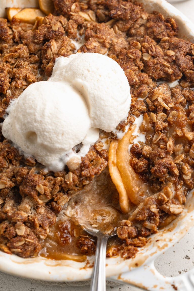gluten free apple crisp in a baking dish with a spoon and two scoops of ice cream on top.