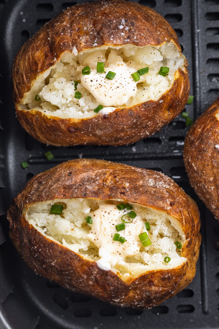 air fryer baked potato in an air fryer basket with butter and chives on top.