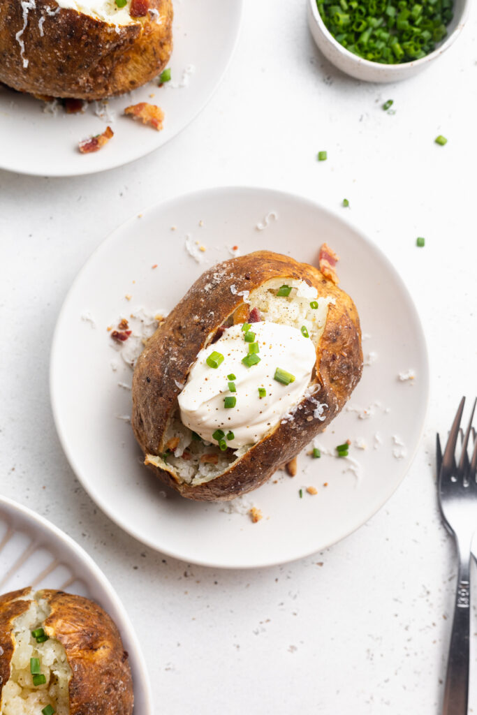 overhead image of a loaded air fryer baked potato with chives on the side.