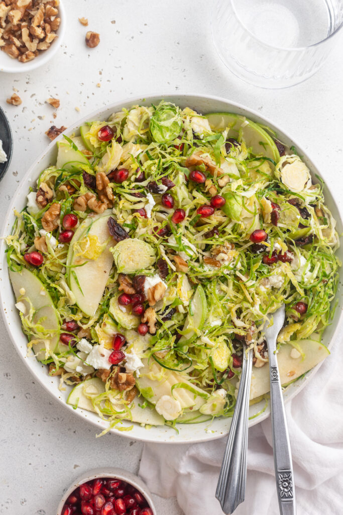 overhead image of brussels sprout salad with walnuts and pomegranate seeds on the side.