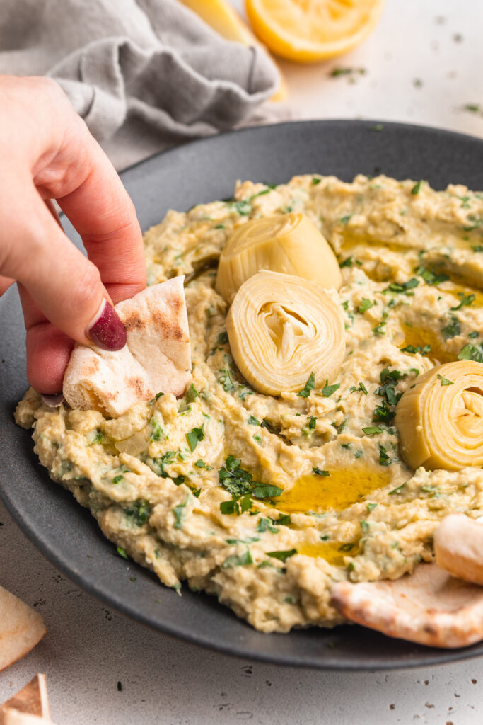 pita being dipped into spinach artichoke hummus.