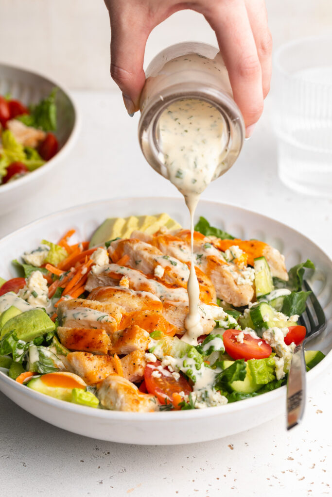 homemade ranch dressing being poured over a buffalo chicken salad.