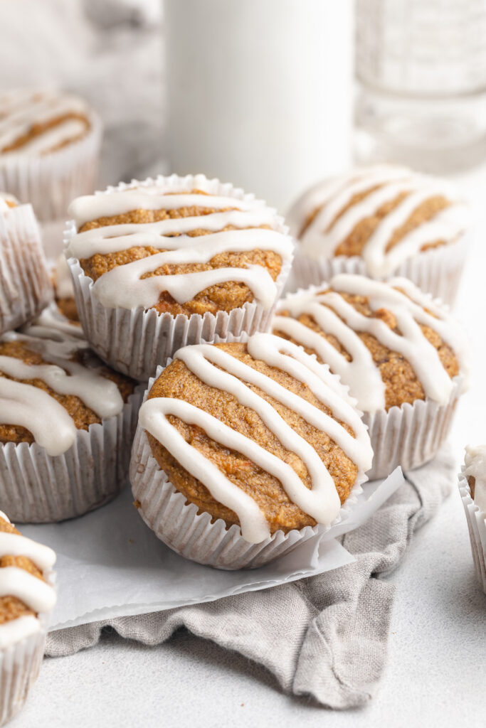 healthy carrot cake muffins with cream cheese icing on top, stacked on top of each other.