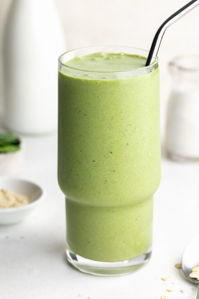 close-up image of a nourishing green lactation smoothie with a metal straw.