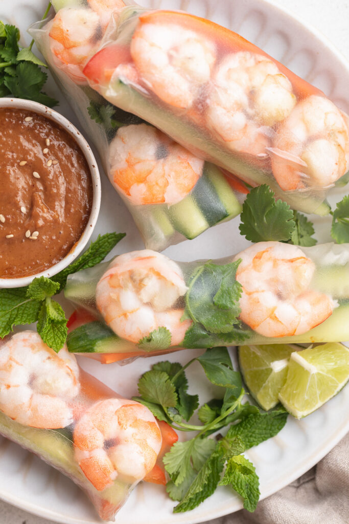 close-up overhead image of shrimp spring rolls on a plate with peanut sauce.