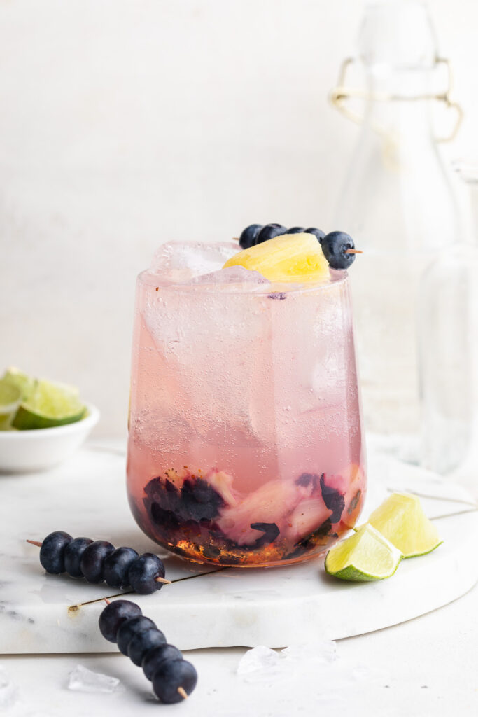 sunset spritz mocktail in a glass with fresh blueberries and pineapple on top.