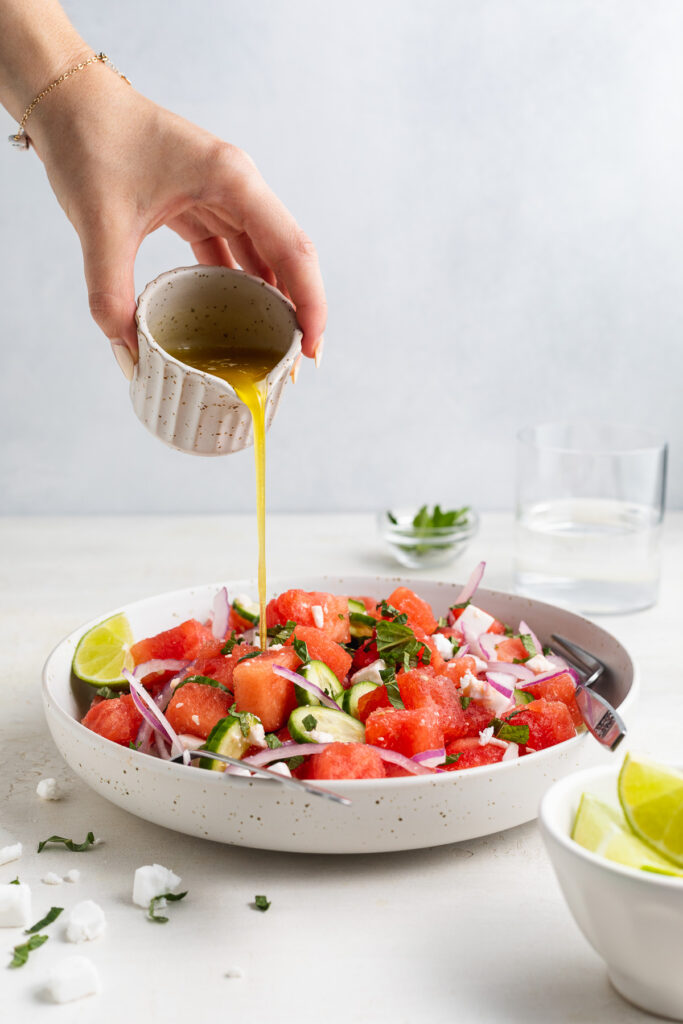 lime dressing being poured over watermelon salad.