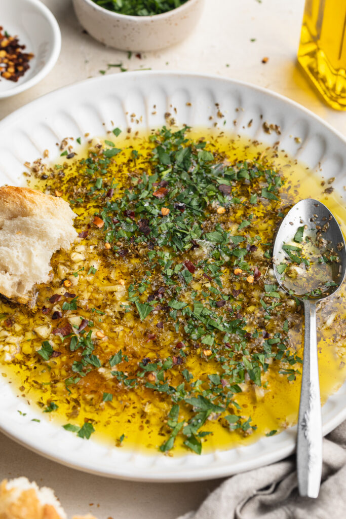 garlic and herb olive oil dip on a plate with bread on the side.