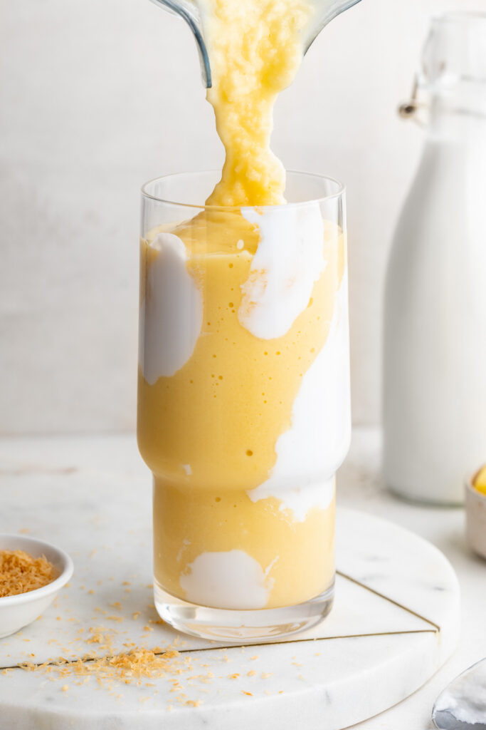 mango pineapple smoothie being poured into a glass.