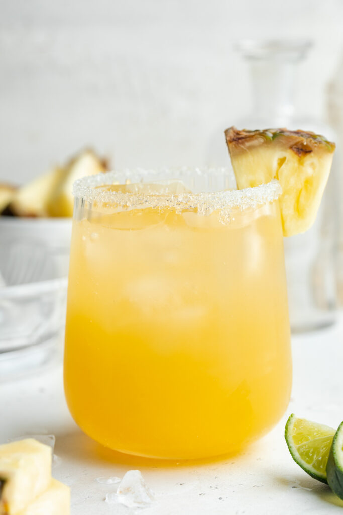 pineapple margarita in a glass with lime wedges on the side.