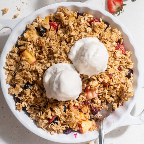 Overhead image of summer fruit crisp in a baking dish with vanilla ice cream on top.
