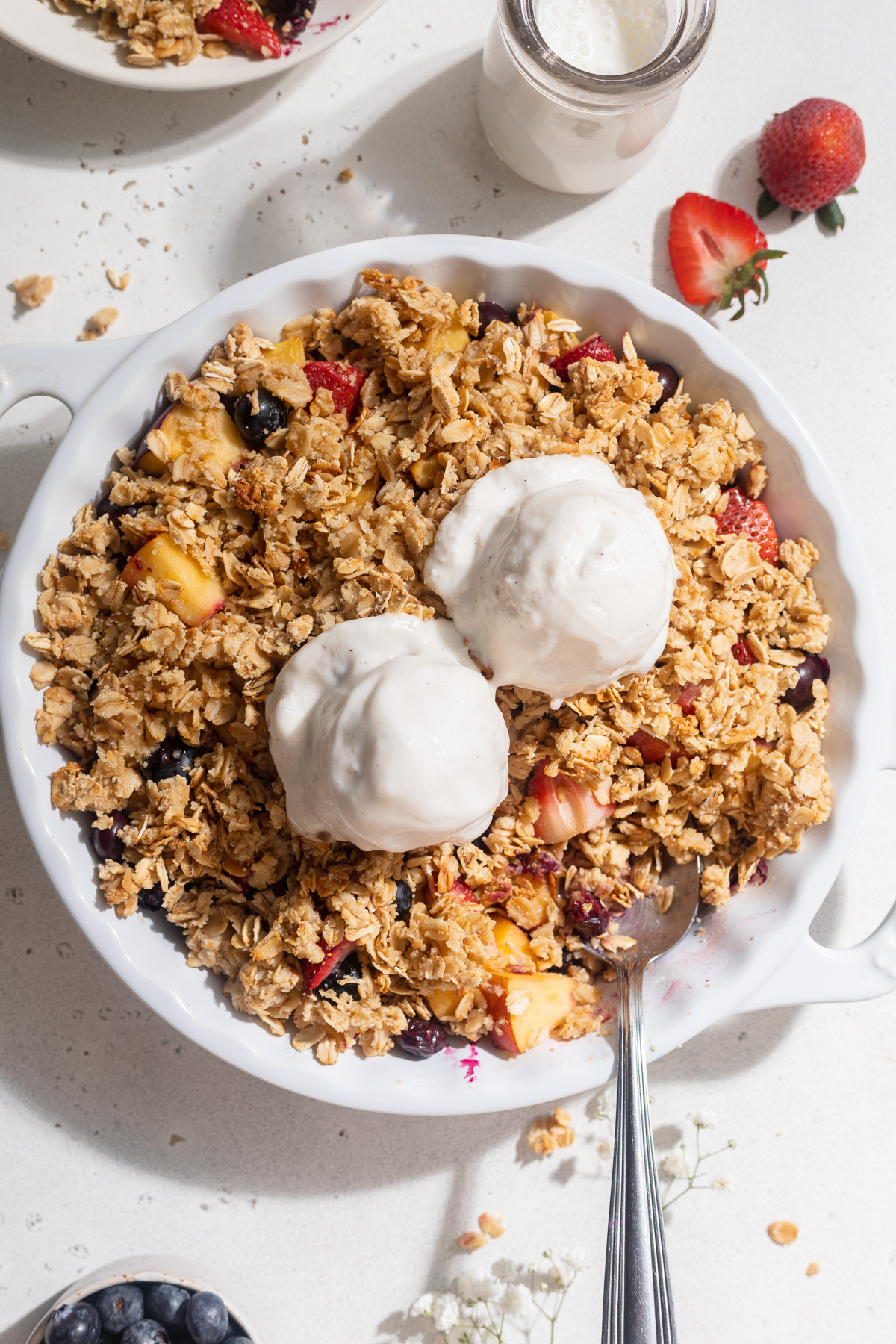 Overhead image of summer fruit crisp in a baking dish with vanilla ice cream on top.